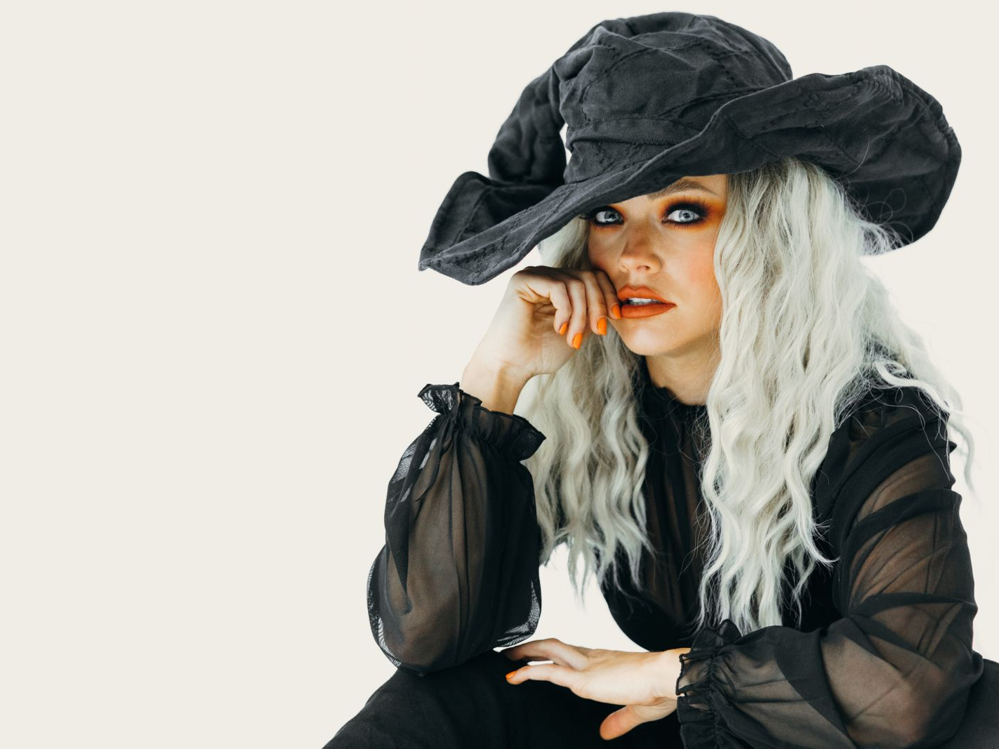 Woman in a black witch costume with orange makeup posing against a light backdrop